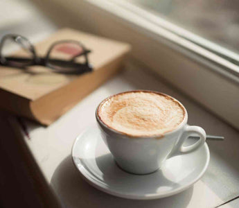 Kaffe neben einem Buch und einer Brille auf einer Fensterbank