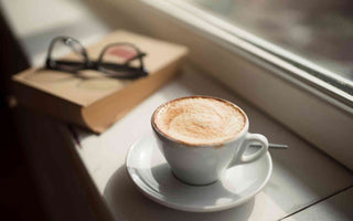 Kaffe neben einem Buch und einer Brille auf einer Fensterbank