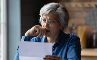ältere Frau mit Brille, die etwas auf einem Blatt Papier liest