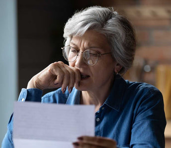 ältere Frau mit Brille, die etwas auf einem Blatt Papier liest